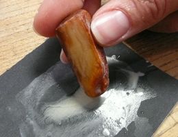 Ein Hand hält ein Stück Holz, das auf einem schwarzen Schleifpapier reibt. Es sind Spuren von Schleifstaub sichtbar.