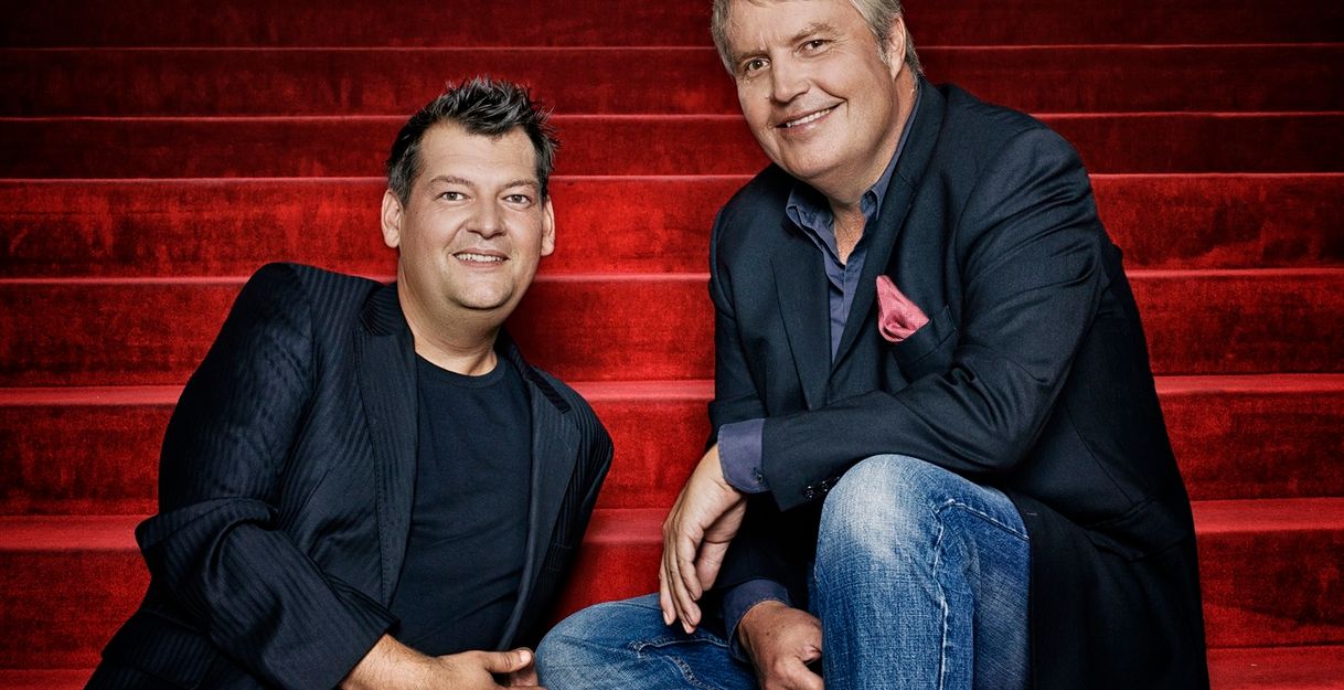 Hans-Jürgen Mende (rechts im Bild) und Philipp Schmid sitzen auf einer roten Treppe und posieren für ein gemeinsames Bild