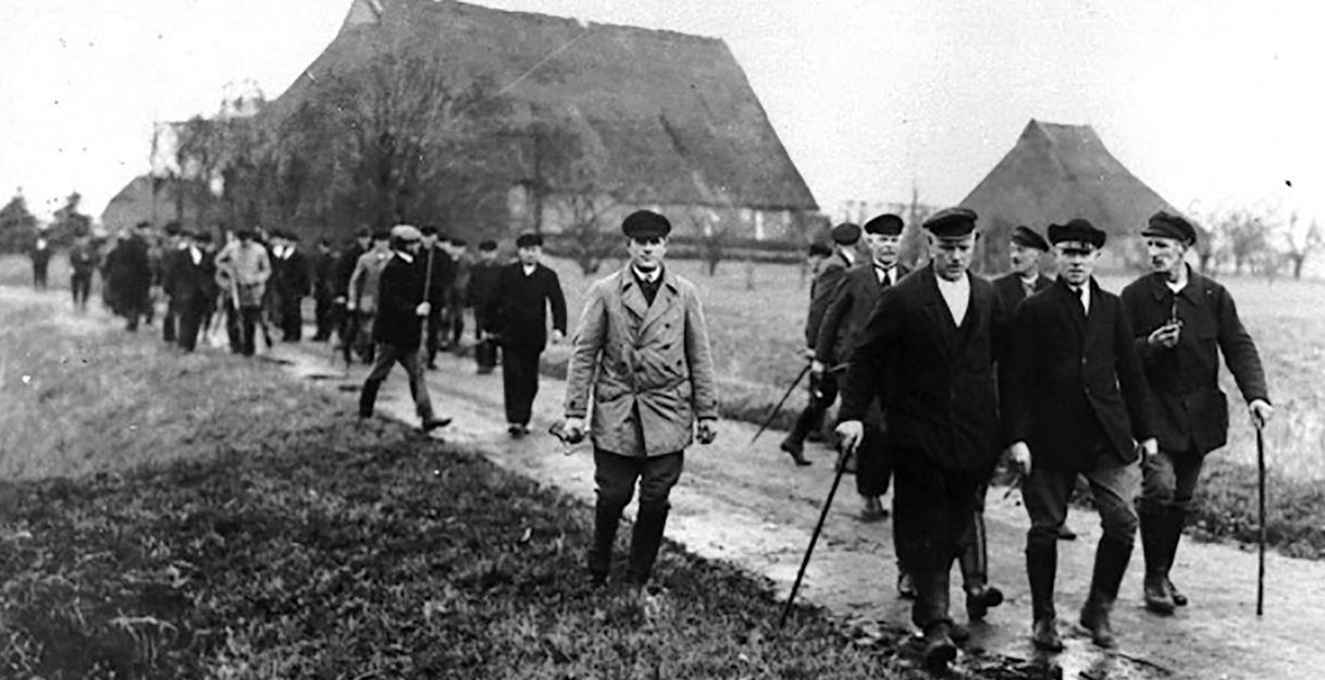 Schwarz-weiß Bild zeigt auf einem Weg laufende Bauern.