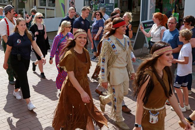 Eine Gruppe von Menschen geht fröhlich auf der Straße. Einige tragen traditionelle Kostüme, während andere normale Kleidung haben.