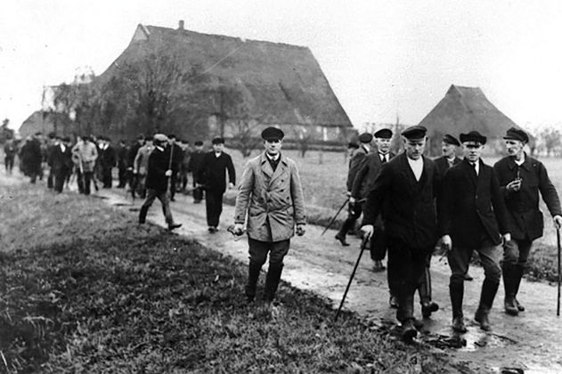 Schwarz-weiß Bild zeigt auf einem Weg laufende Bauern.